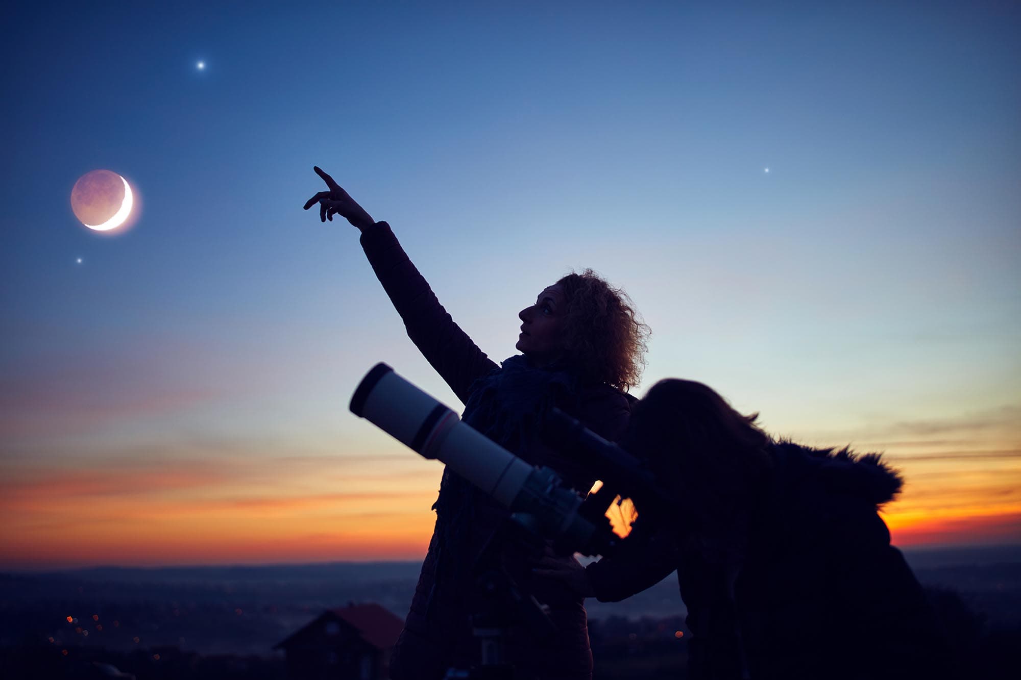 Silhouetted people stargazing at a crescent moon